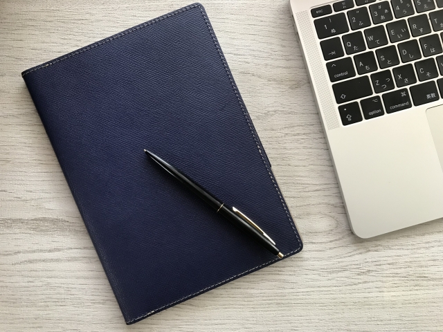 企業法務のイメージ（手帳・ペン・ノートパソコン）